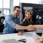 Male customer and female car dealer shaking hands at showroom