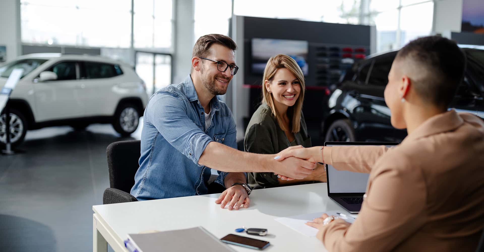 Male customer and female car dealer shaking hands at showroom