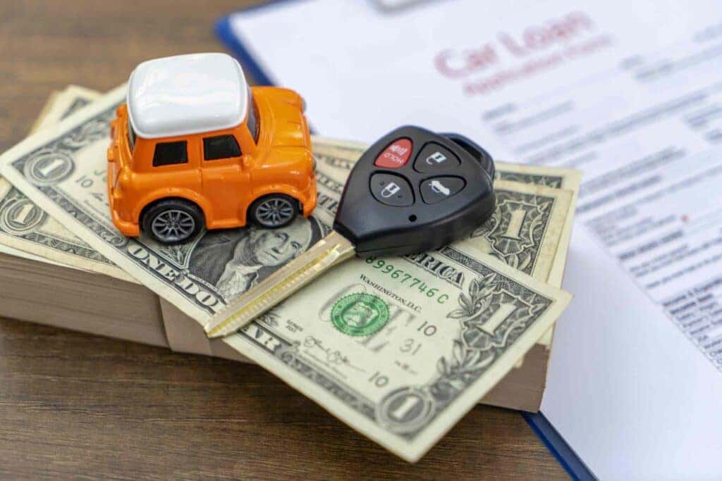 A Cute Orange Toy Car And A Car Key Laying On A Stack Of Dollar Bills