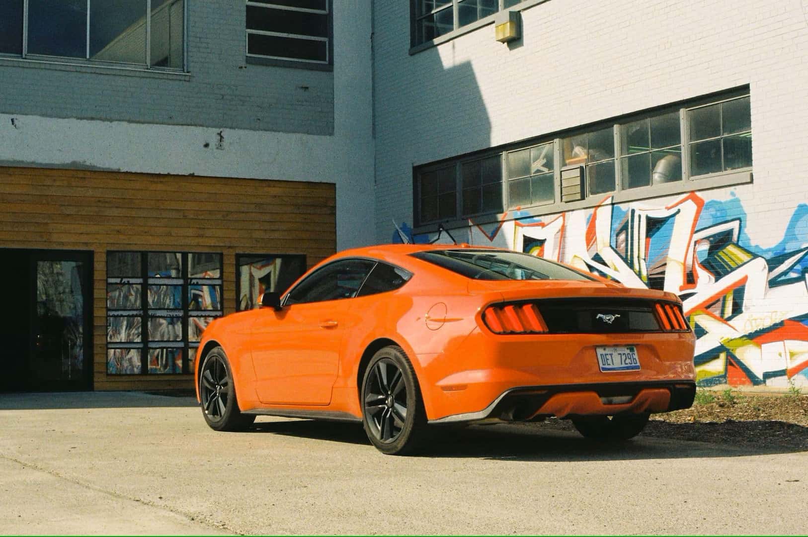 An Orange 2015 Ford Mustang Back Profile Parked Near A Beautiful Building