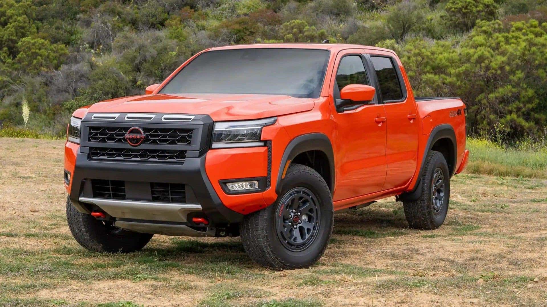 The Attractive Red Exterior Of The Astounding 2025 Nissan Frontier, Parked On The Grass Near A Enchanting Forest