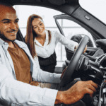 A Customer In The Driver's Seat, Helped By A Dealership Employee, Taking The Car On A Test Drive