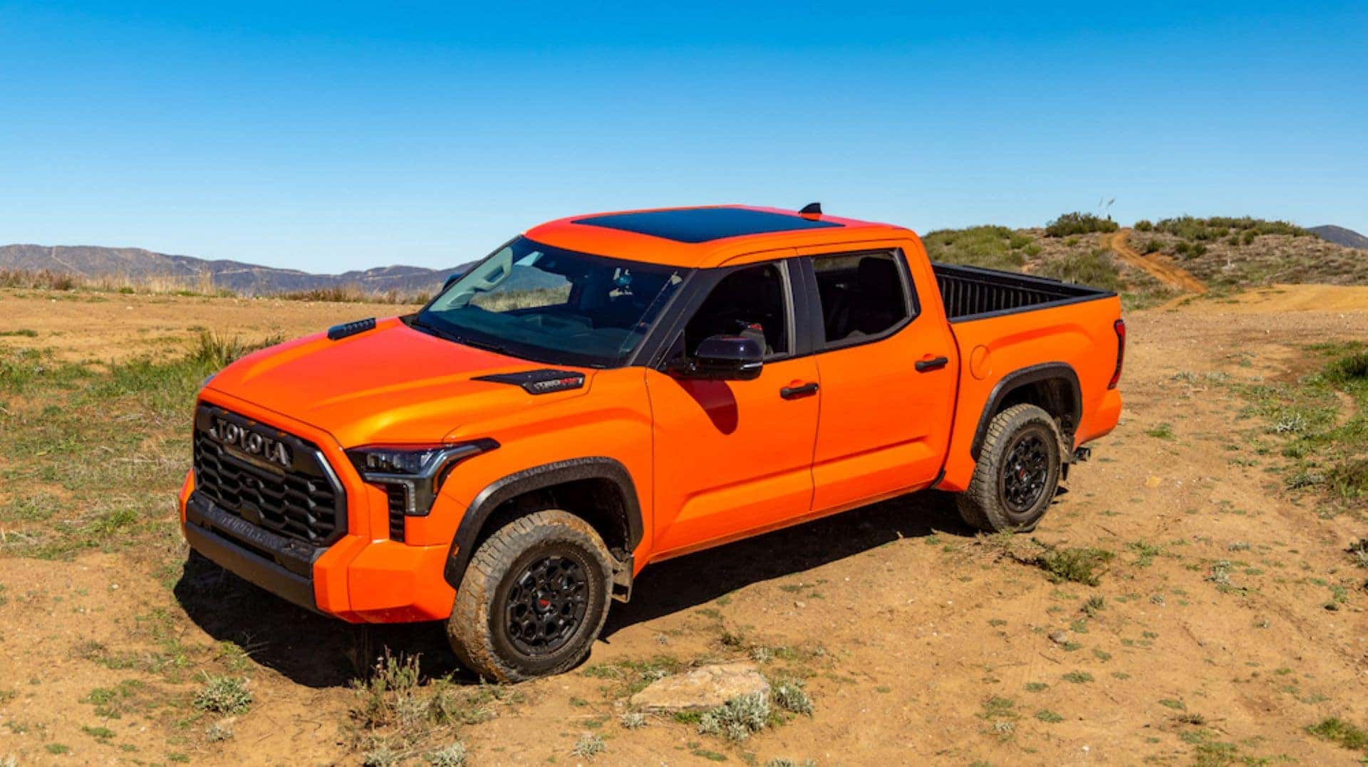 An Orange Tundra TRD Pro, Driving In Half Dirt Half Grass Terrain