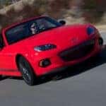The Agile And Affordable Sports Car: the Mazda MX-5 Miata, Speeding On The Highway Past Bushy Greenery