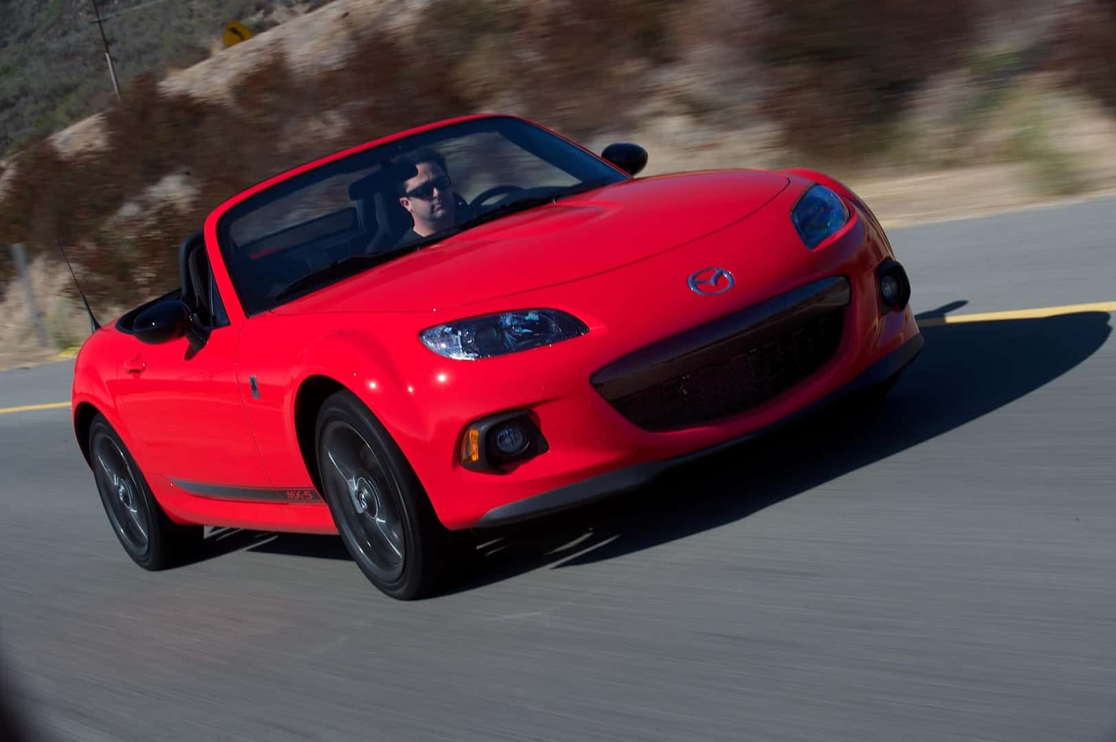 The Agile And Affordable Sports Car: the Mazda MX-5 Miata, Speeding On The Highway Past Bushy Greenery