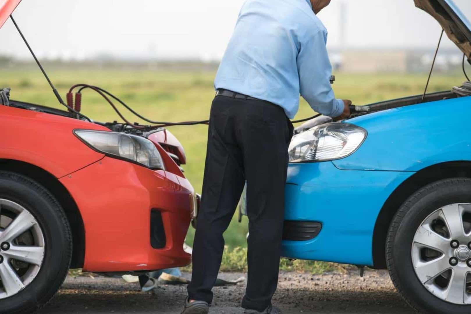 A Man Jumpstarting His Car's Battery By Connecting It To Another Car's Battery