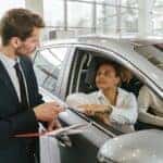 Car Dealer Handing in Keys to a Woman Sitting in a New Car