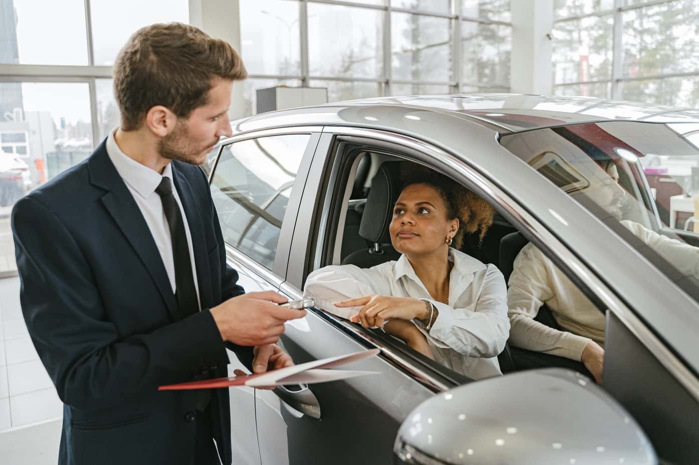 Car dealer handing keys to a woman sitting in a new car