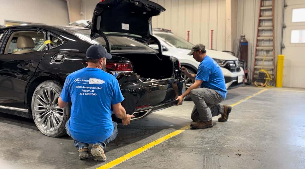 Two men putting a bumper on a car