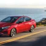 Red Nissan Versa driving on a road with the ocean in the background