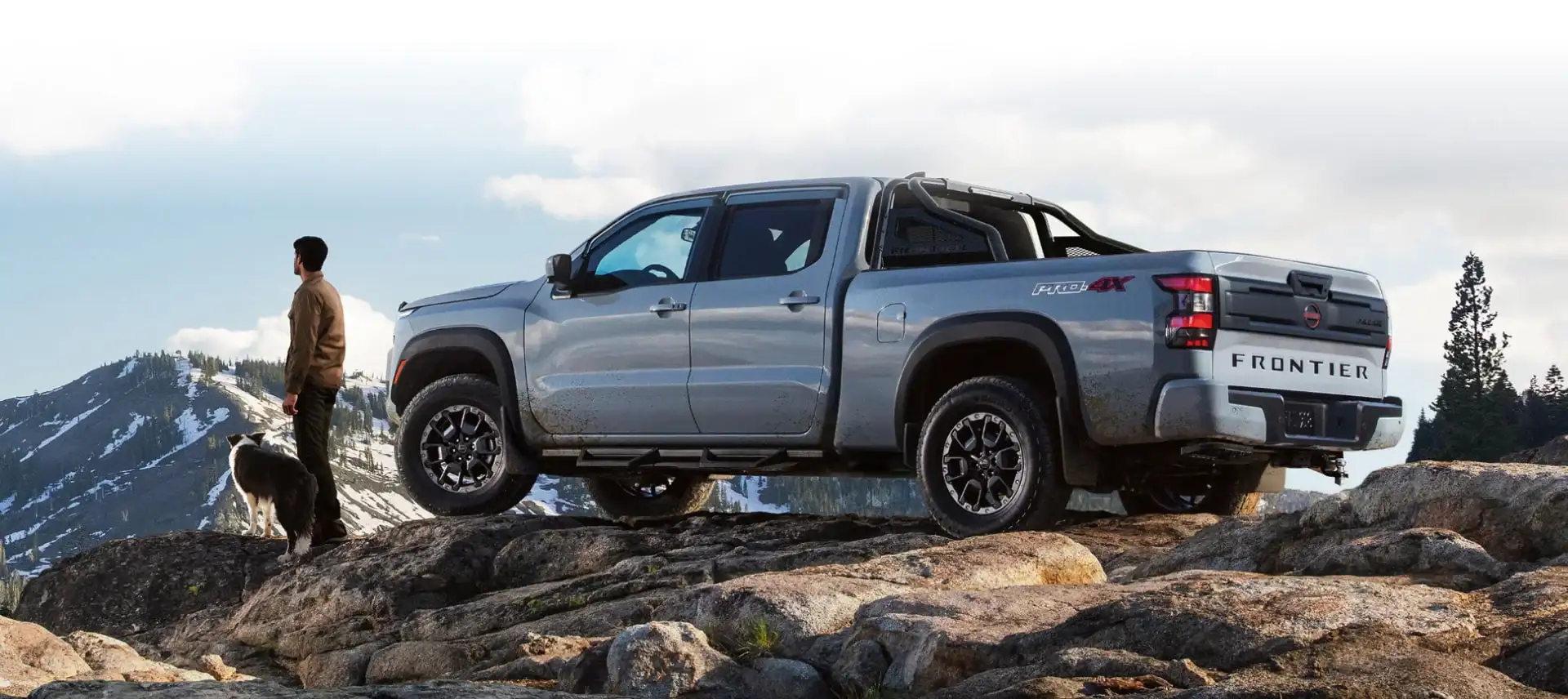 Man and dog standing in front of 2025 Nissan Frontier on a rocky mountain