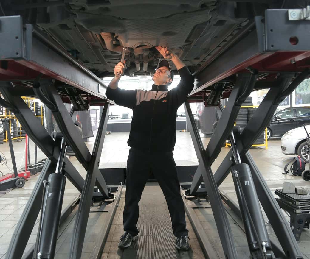 Man in black jacket and black pants standing under vehicle