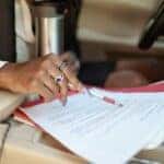 Person Wearing Silver Ring Holding Red Pen on White Printer Paper