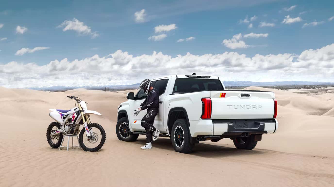 Person standing next to a Toyota Tundra in riding gear on sand dunes