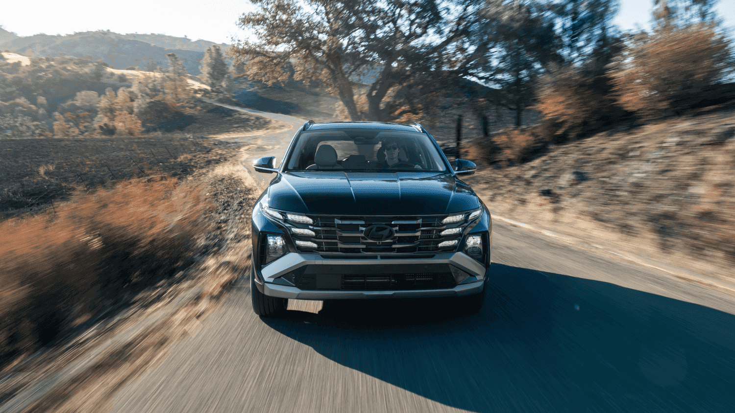 Bold front profile of the 2025 Hyundai Tucson Hybrid driving through scenic Athens, GA roads, showcasing its eco-friendly performance.
