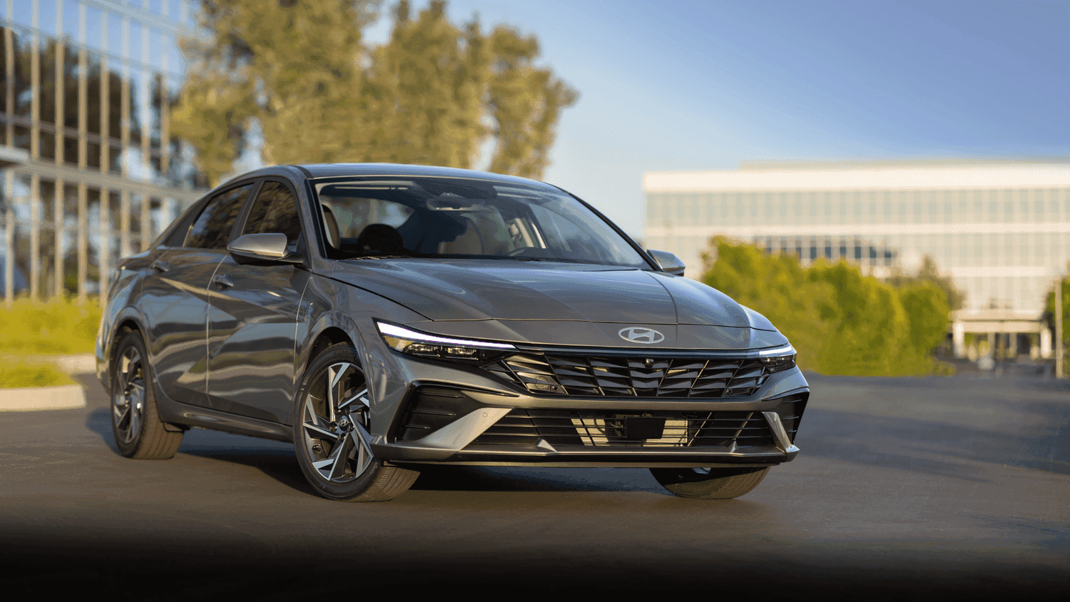 Front angle of the 2025 Hyundai Elantra in Athens, GA, parked outside a modern office complex, emphasizing its sleek lines and sharp LED headlights.