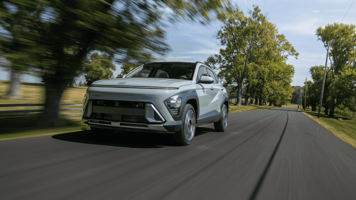 2025 Hyundai Kona compact SUV driving through tree-lined roads near Loganville, GA, designed with family-friendly features.
