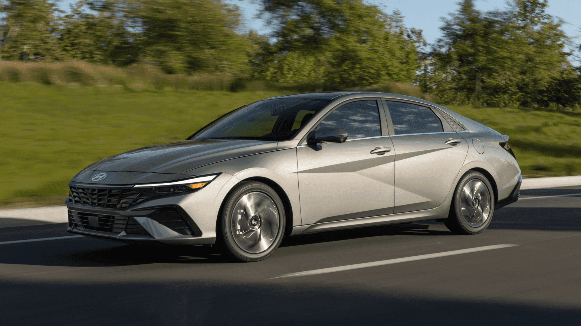 2025 Hyundai Elantra side-front angle in motion, silver finish, daytime driving on clear roadway.