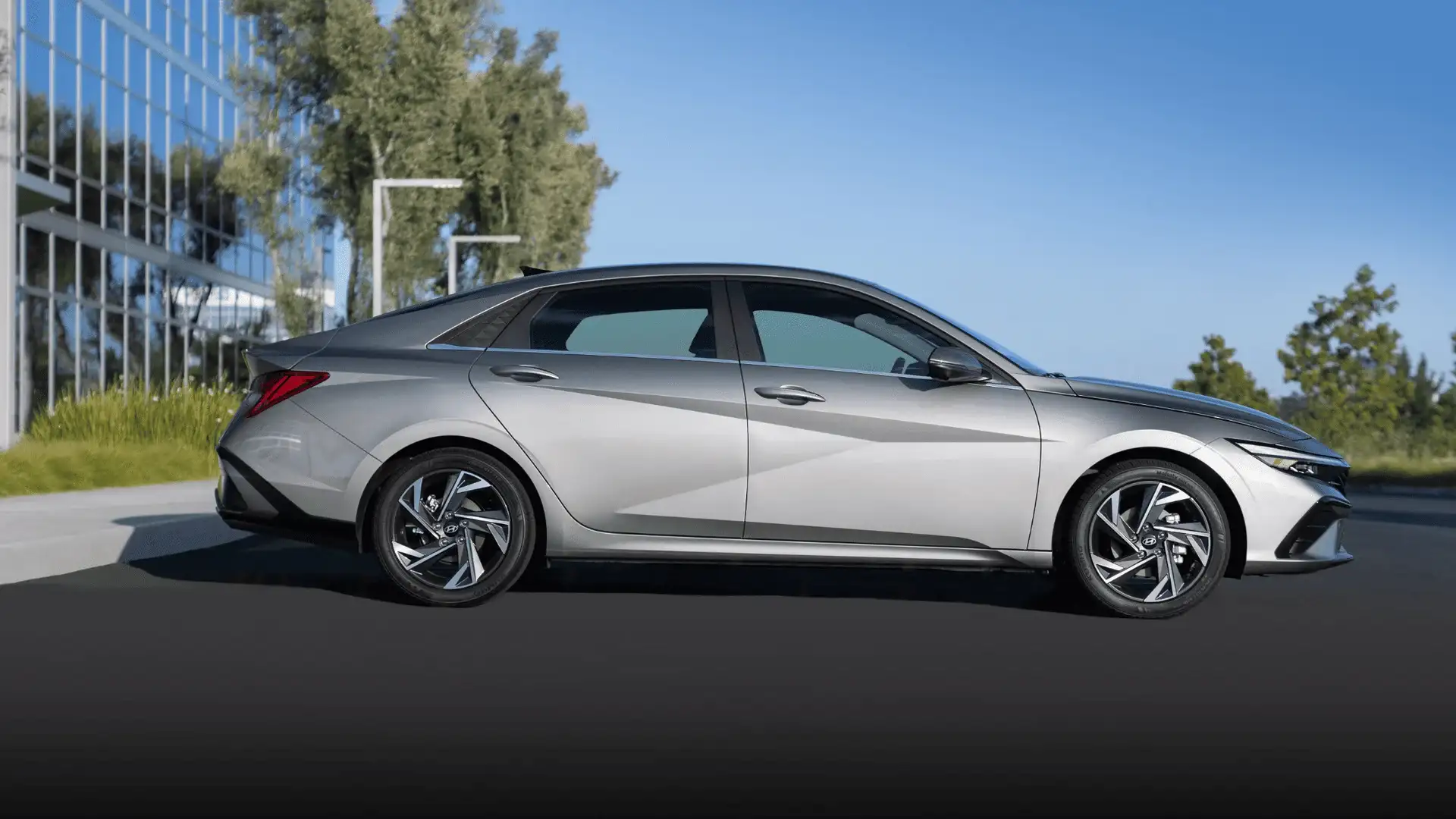Side view of 2025 Hyundai Elantra in silver parked beside a modern building, showing angular body lines and alloy wheels.