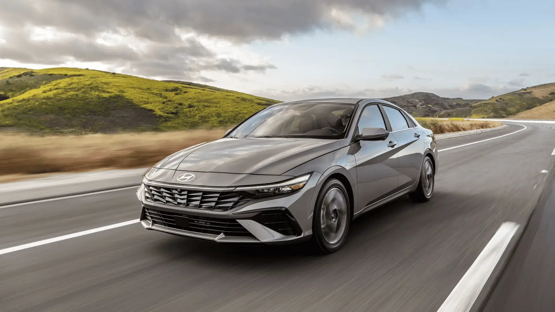Front-side angle of 2025 Hyundai Elantra in motion on a winding road, highlighting the sharp grille and sleek headlights.