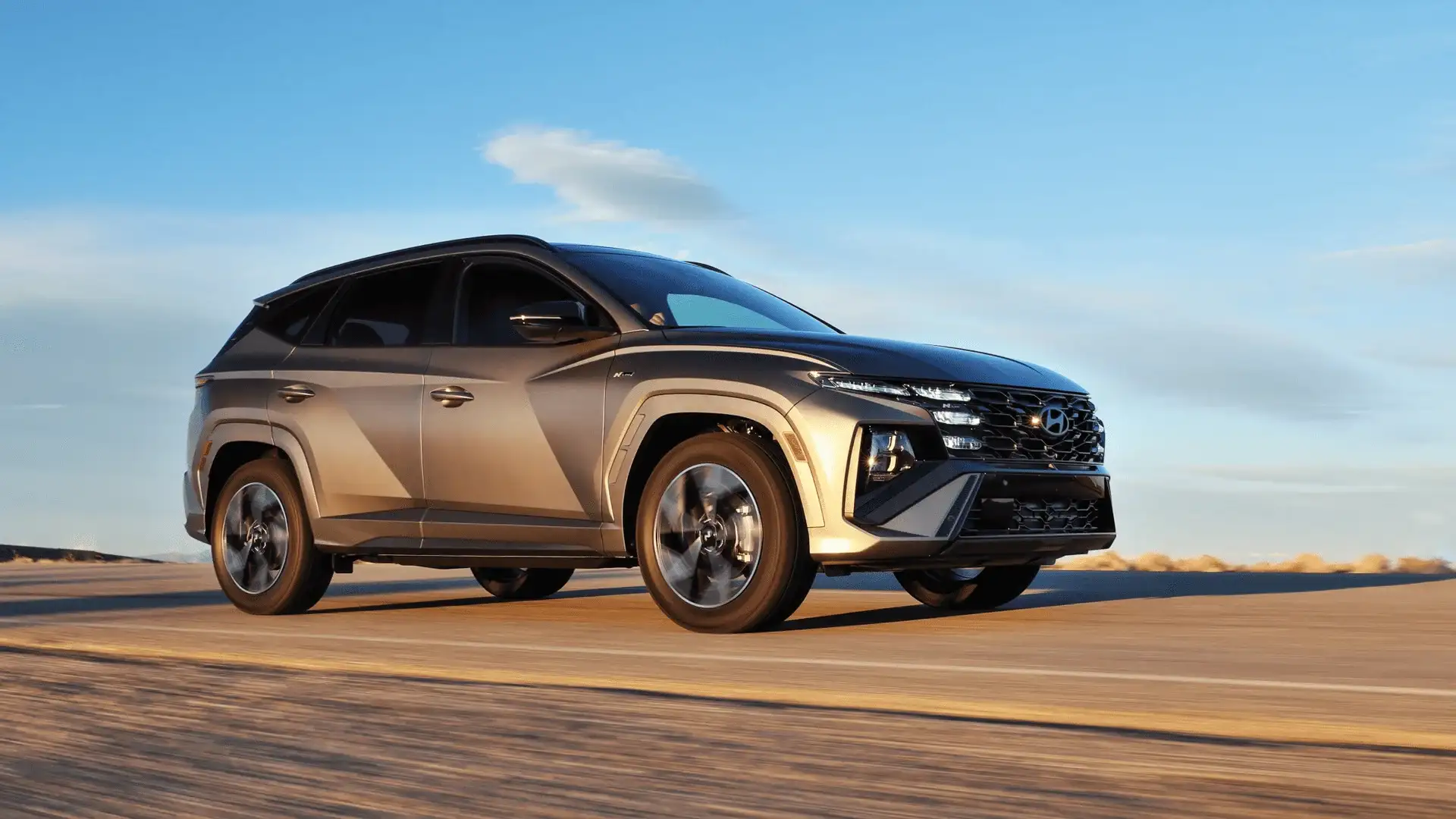 Front-side shot of 2025 Hyundai Tucson in silver on desert road at sunset with dynamic body lines and large alloy wheels.