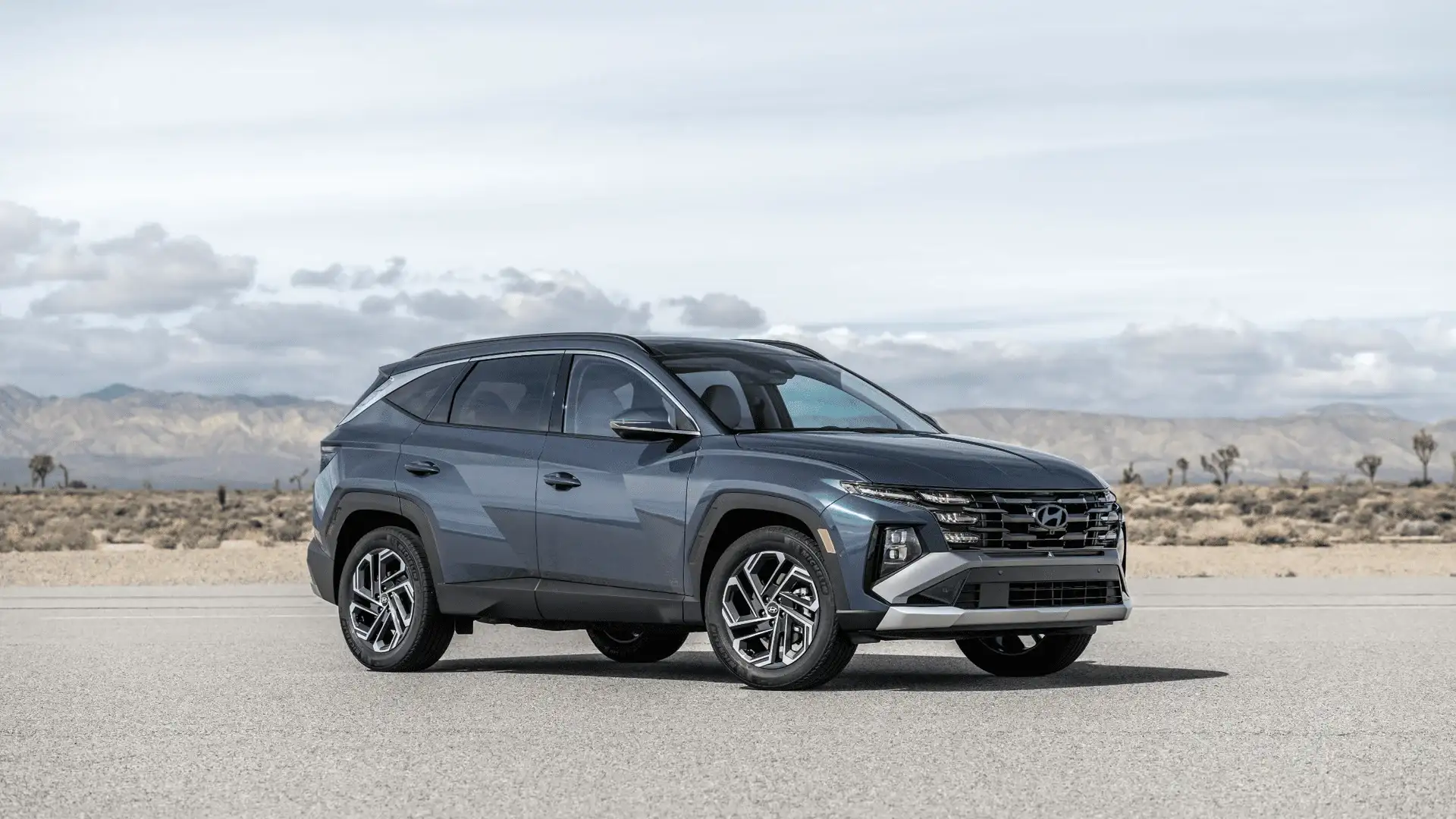 Front three-quarter view of 2025 Hyundai Tucson parked on open desert road with bold grille and LED headlights.