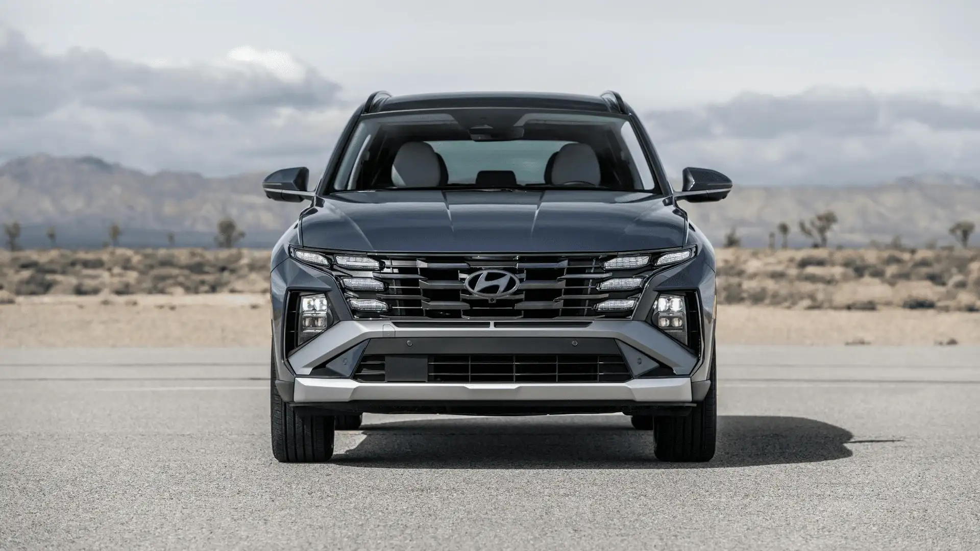 Frontal view of 2025 Hyundai Tucson in gray metallic finish, showcasing split LED lighting and wide grille design.