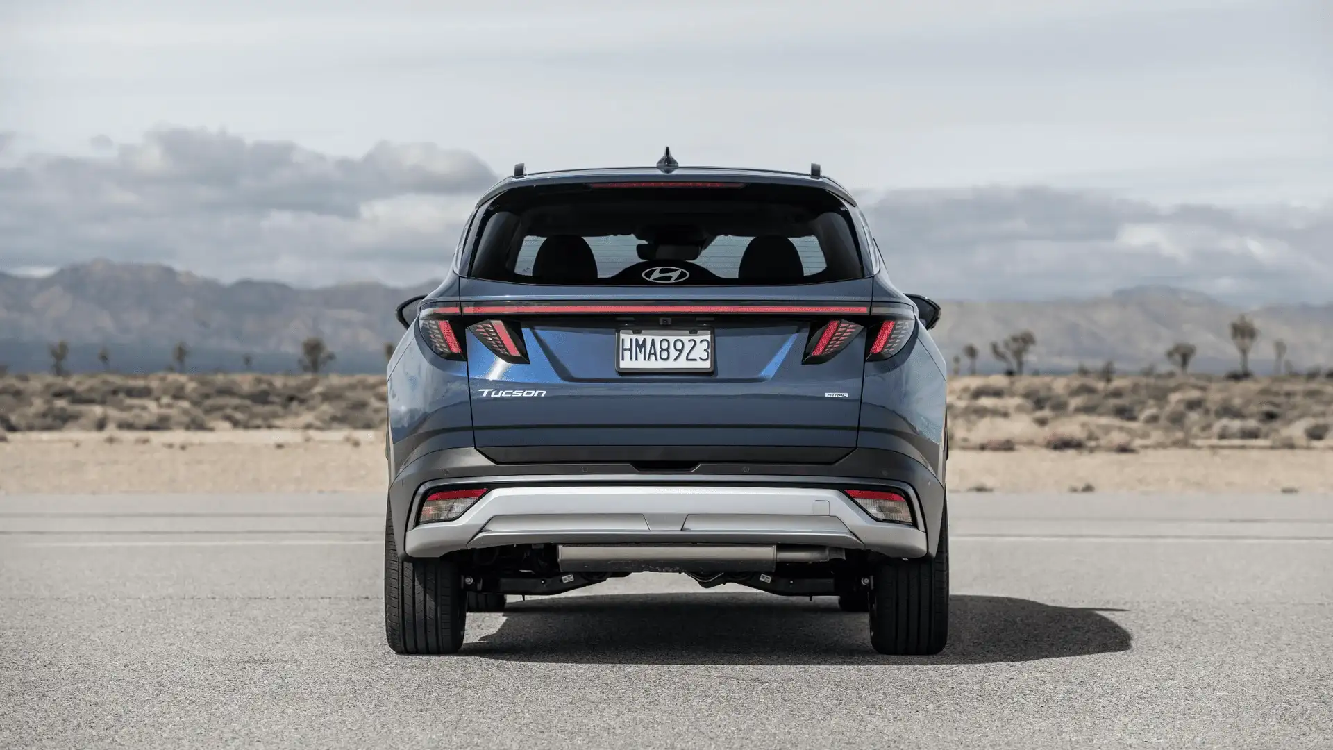 Rear view of the 2025 Hyundai Tucson in blue with full-width taillights and Tucson badging, desert background.