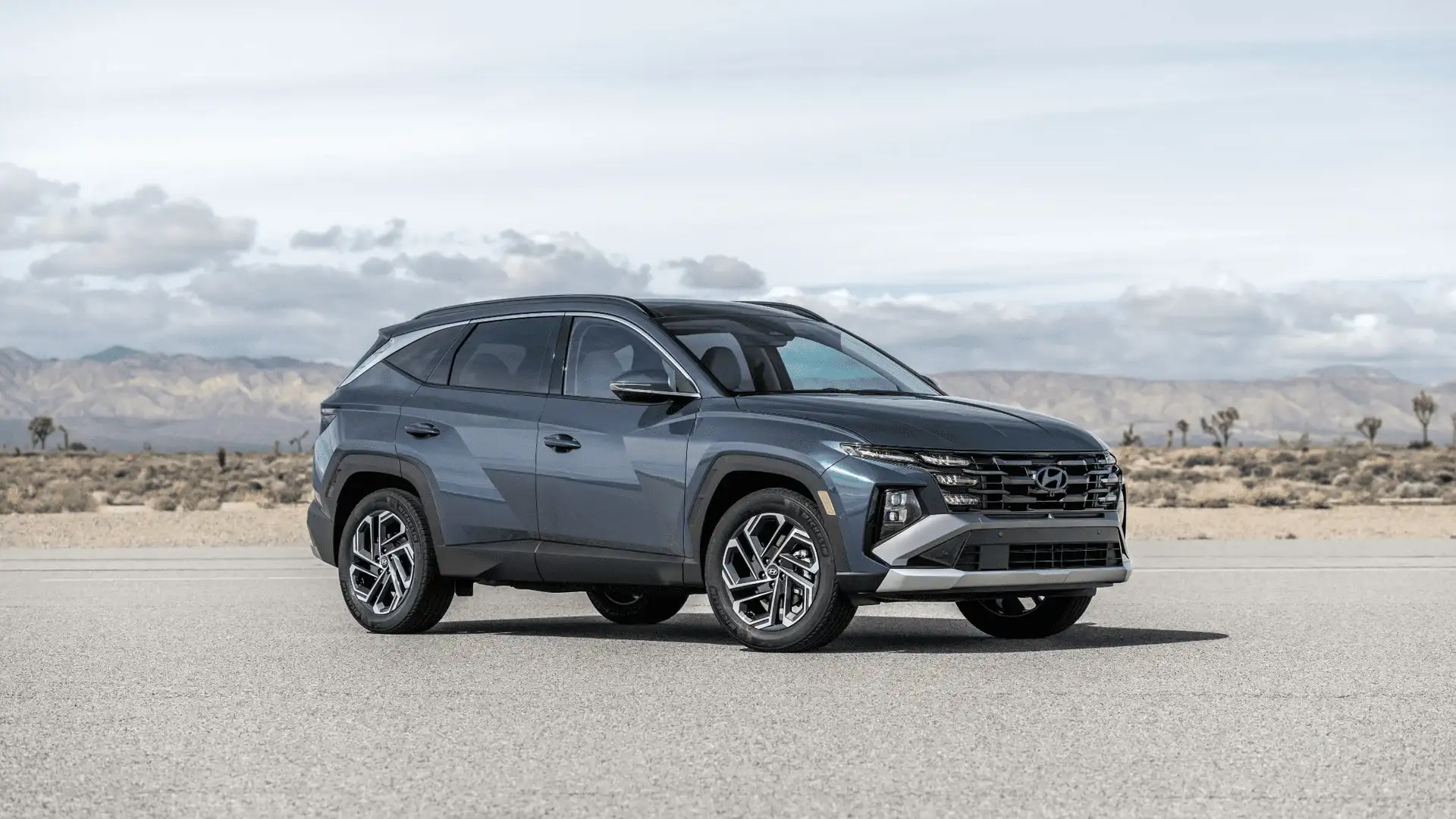 Three-quarter front view of a blue 2025 Hyundai Tucson SUV with angular body lines on a desert highway.
