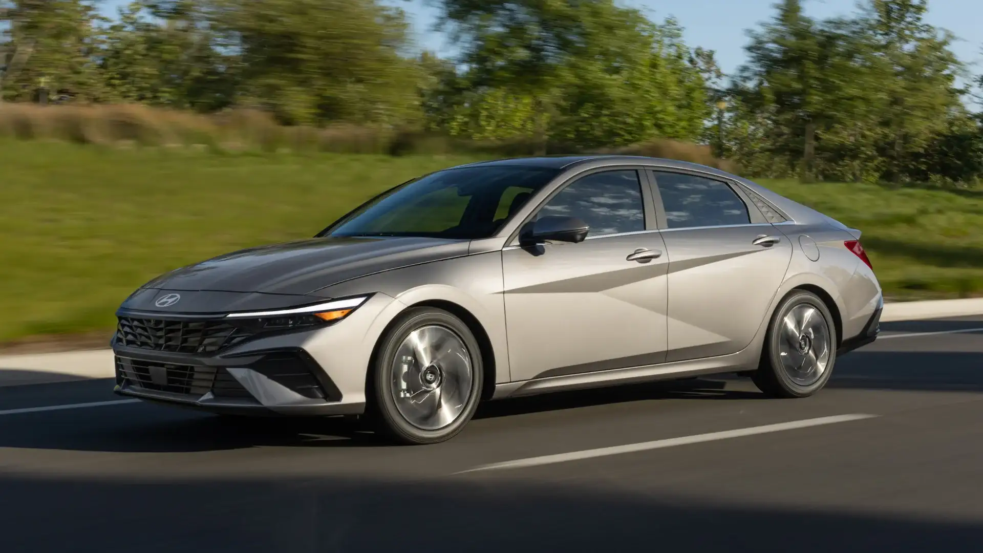 2026 Hyundai Elantra exterior in silver driving on road with sharp body lines and alloy wheels.