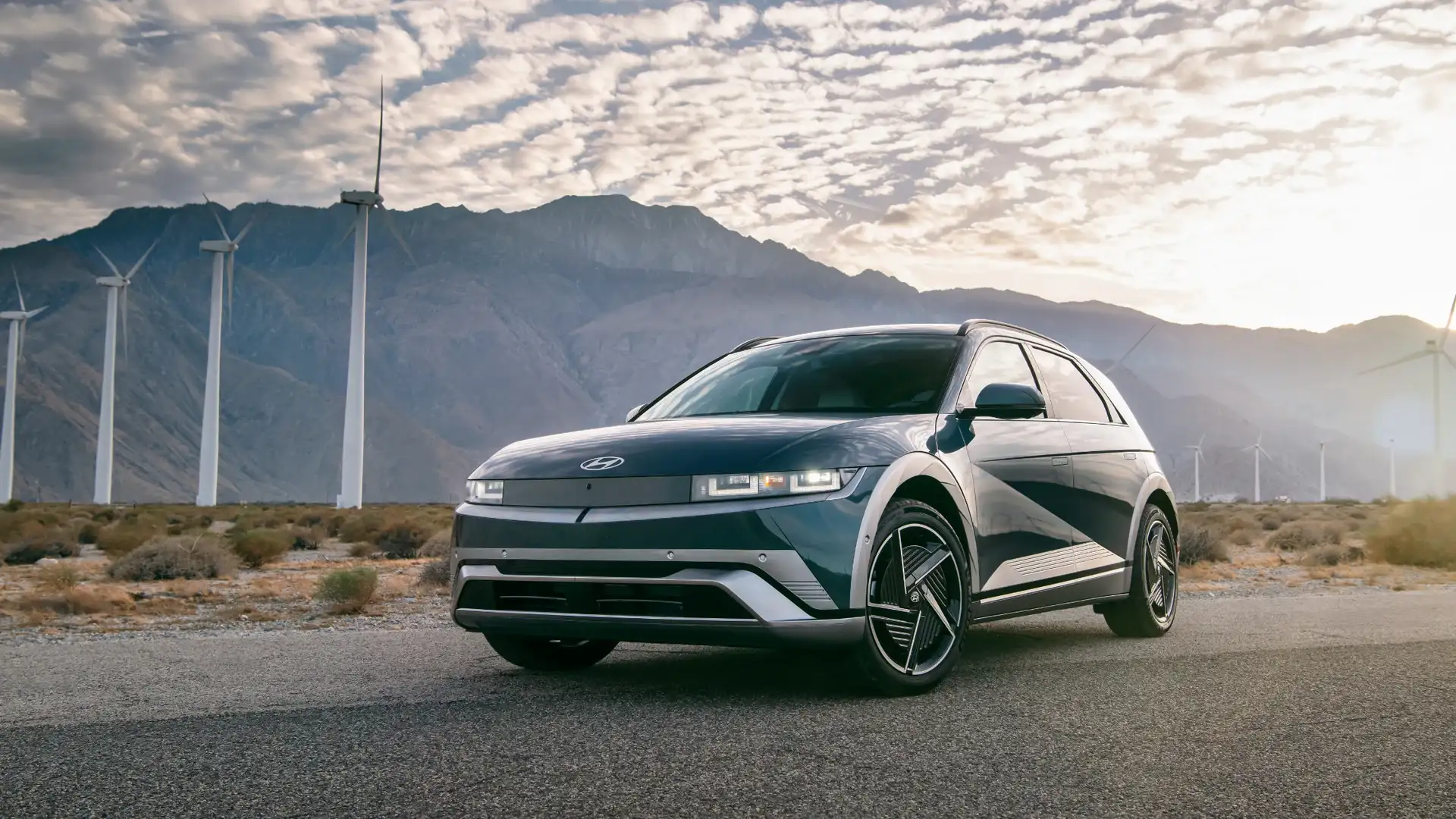 2026 Hyundai IONIQ 5 electric SUV parked in desert landscape with wind turbines, highlighting bold geometric design and pixel LED headlights.