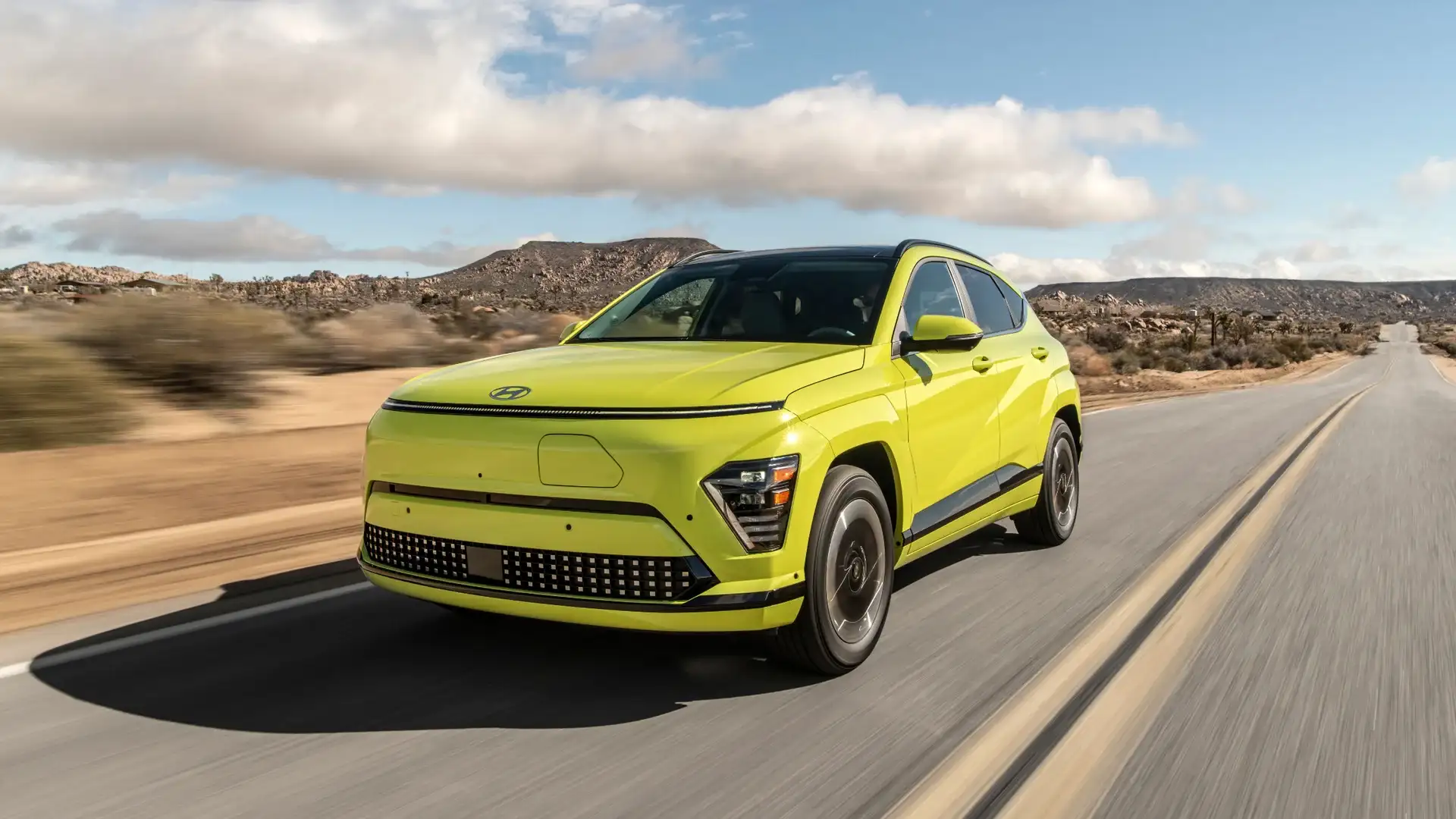 2026 Hyundai Kona Electric in bright yellow driving on desert road with bold front design and LED lights.