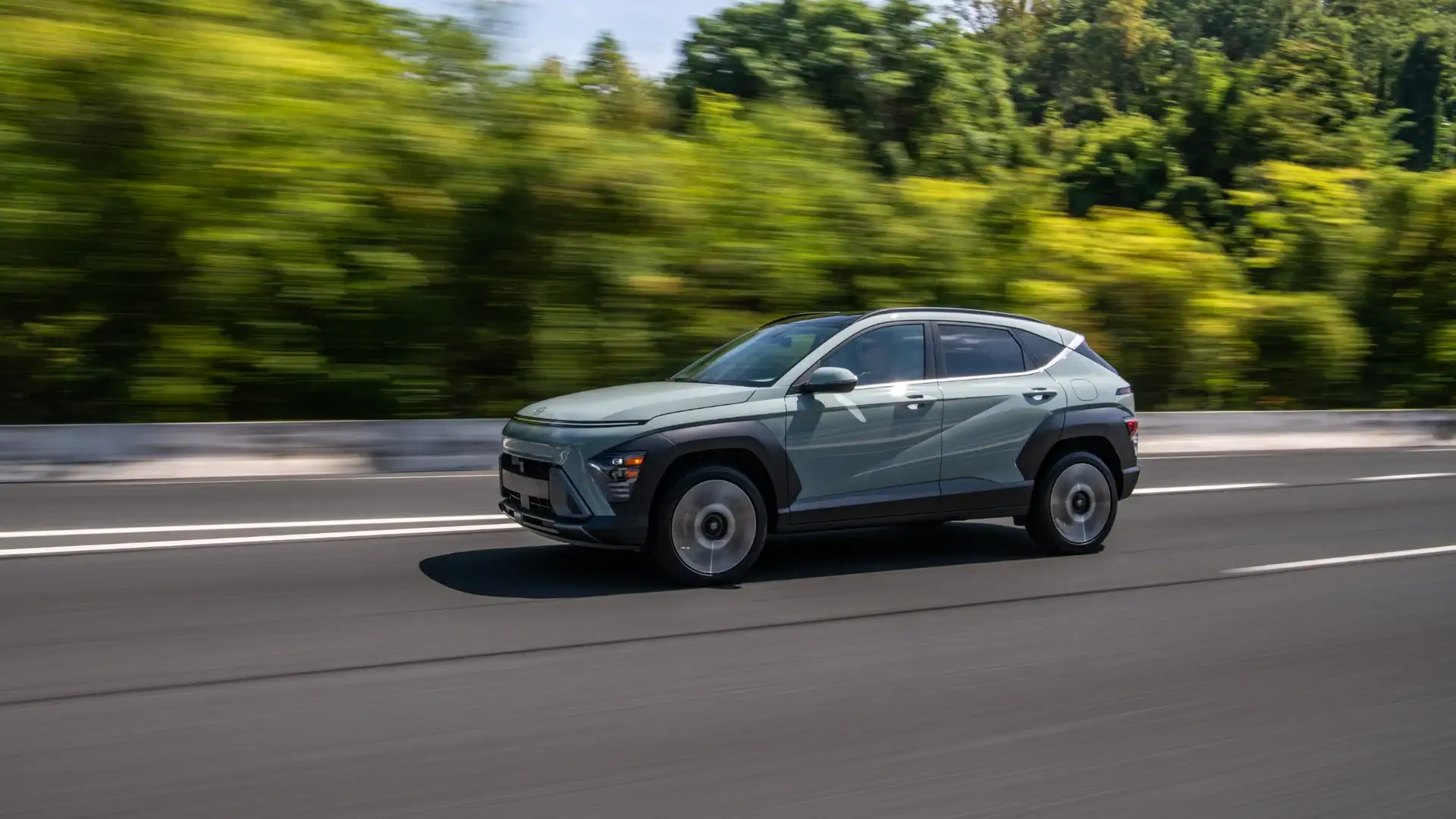 2026 Hyundai Kona in green driving on highway, showcasing aerodynamic side profile and alloy wheels.