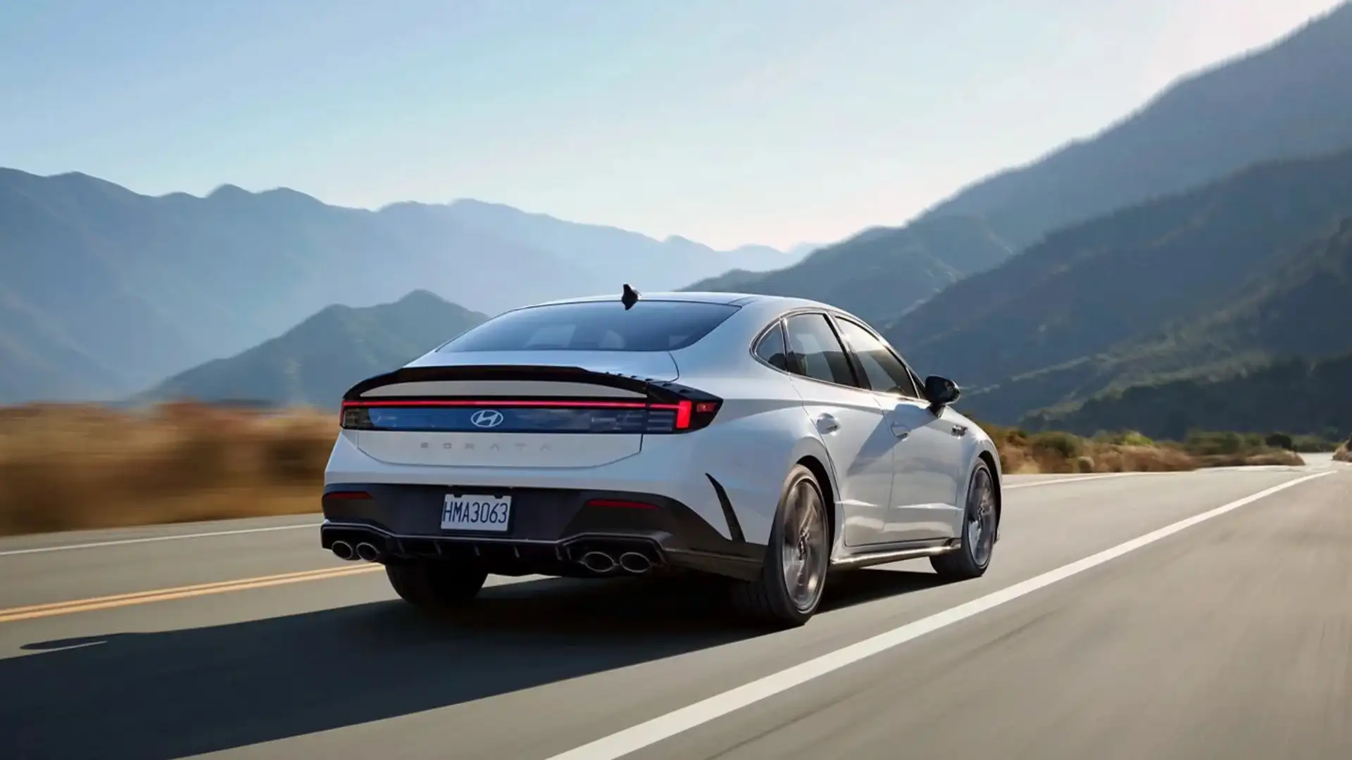 2026 Hyundai Sonata rear view in white driving on highway with LED taillights and quad exhaust.