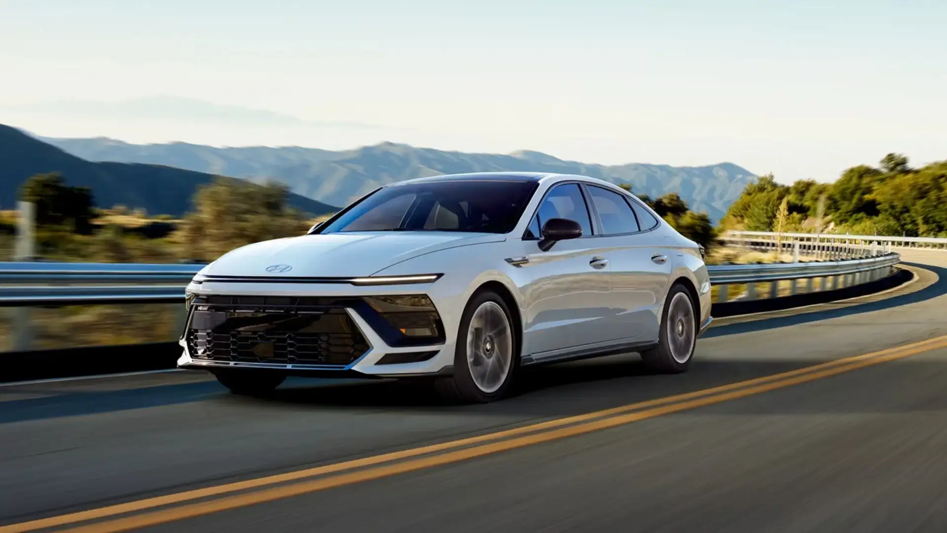 2026 Hyundai Sonata exterior in white driving on winding road with sleek front grille and slim headlights.