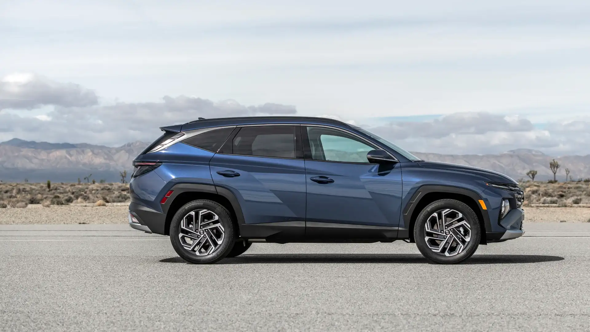 2026 Hyundai Tucson side profile in blue with sharp body lines, alloy wheels, and modern styling.