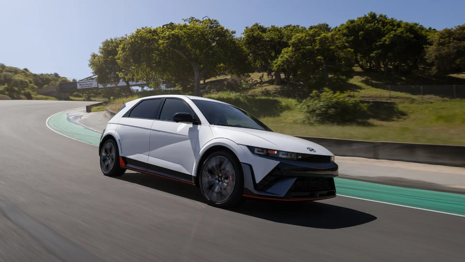 Side view of a white 2025 Hyundai IONIQ 5 N electric crossover driving on a racetrack, showcasing its aerodynamic design and performance-focused styling.