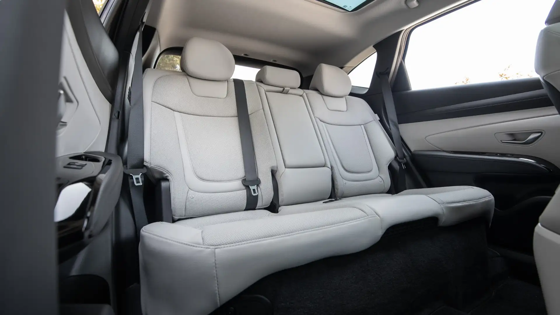 Rear passenger view of the 2025 Hyundai Tucson Hybrid showcasing spacious light gray leather seats, seatbelt setup, and wide cabin comfort.