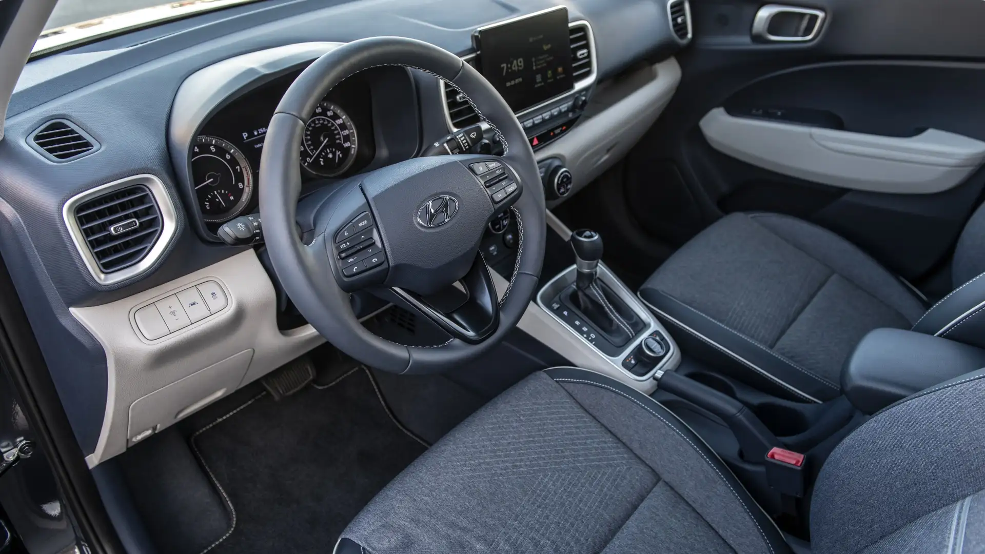Interior cabin of the 2026 Hyundai Venue featuring a black and beige dashboard, touchscreen display, multifunction steering wheel, and comfortable fabric seats.