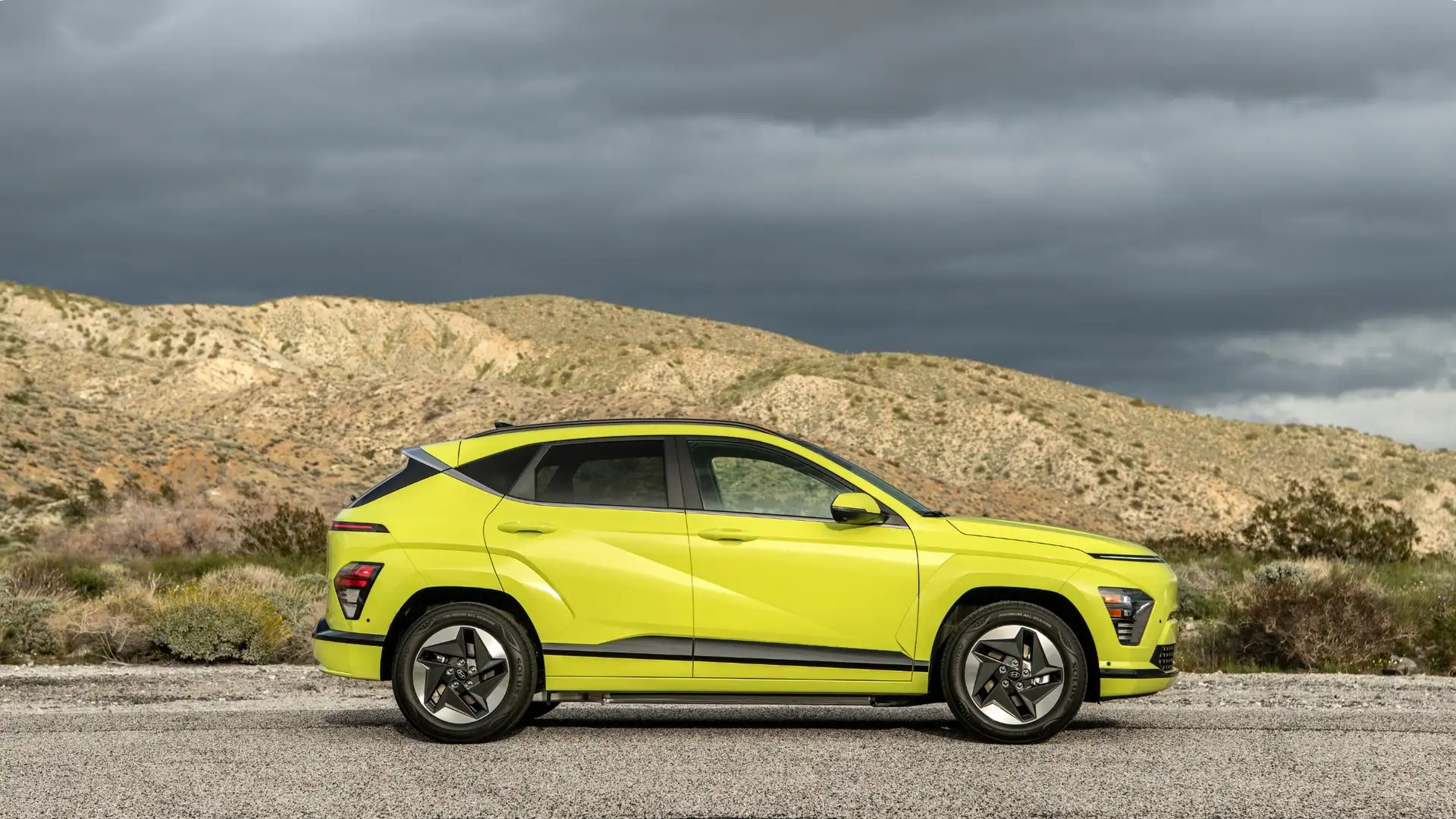 2025 Hyundai Kona Electric in bright green shown in a side profile on a desert road with sculpted body lines.