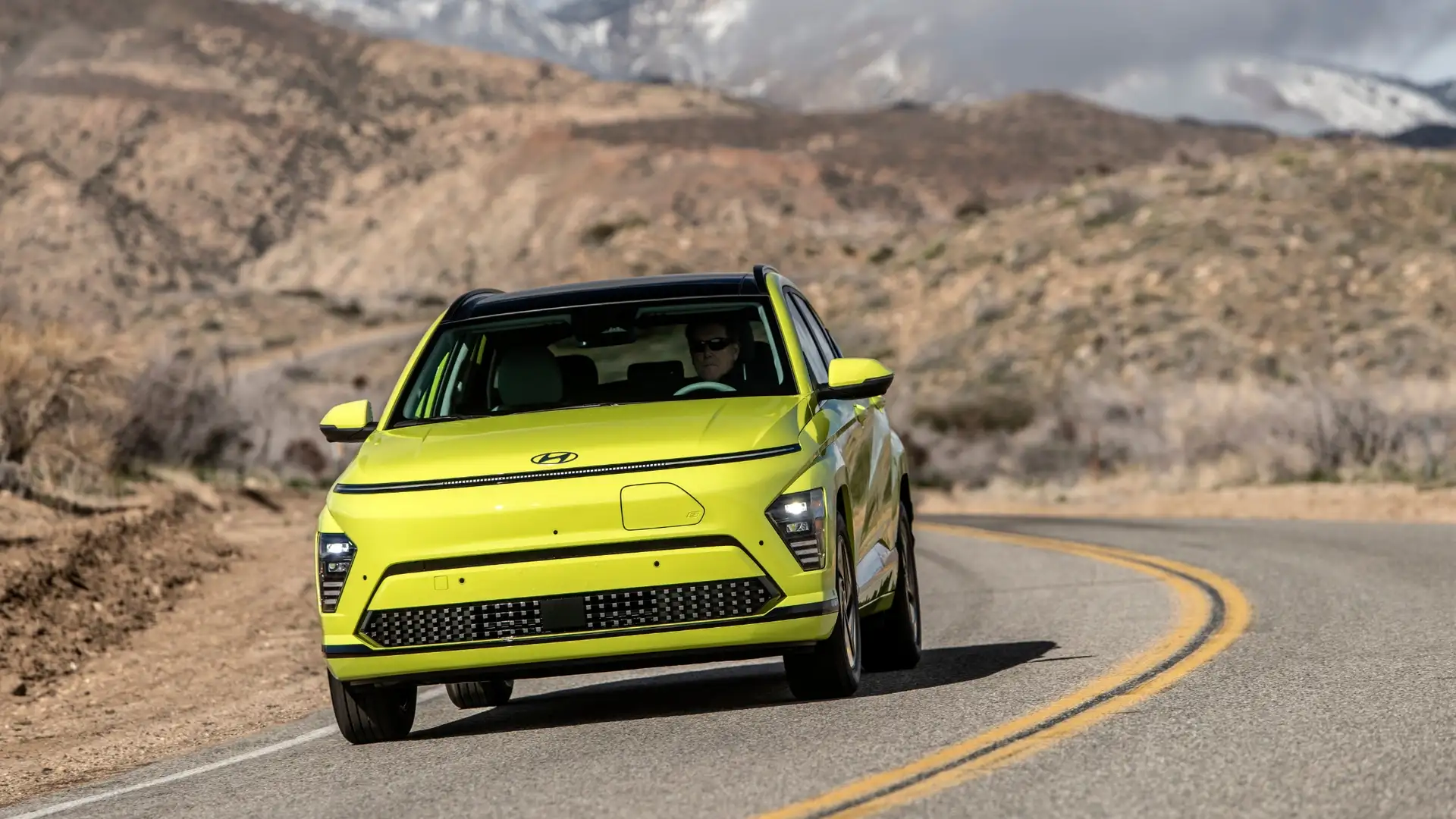 2025 Hyundai Kona Electric driving on a winding mountain road with bold yellow exterior and modern LED lighting.