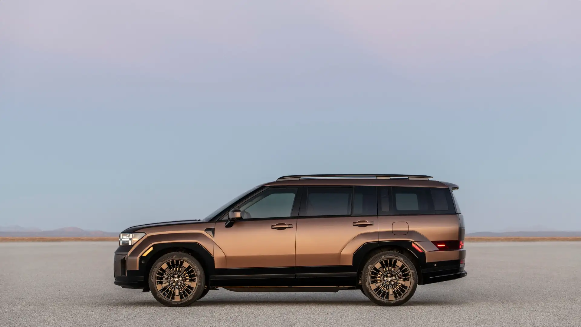 2026 Hyundai Santa Fe Hybrid side profile in bronze finish parked on open terrain under soft sky lighting.