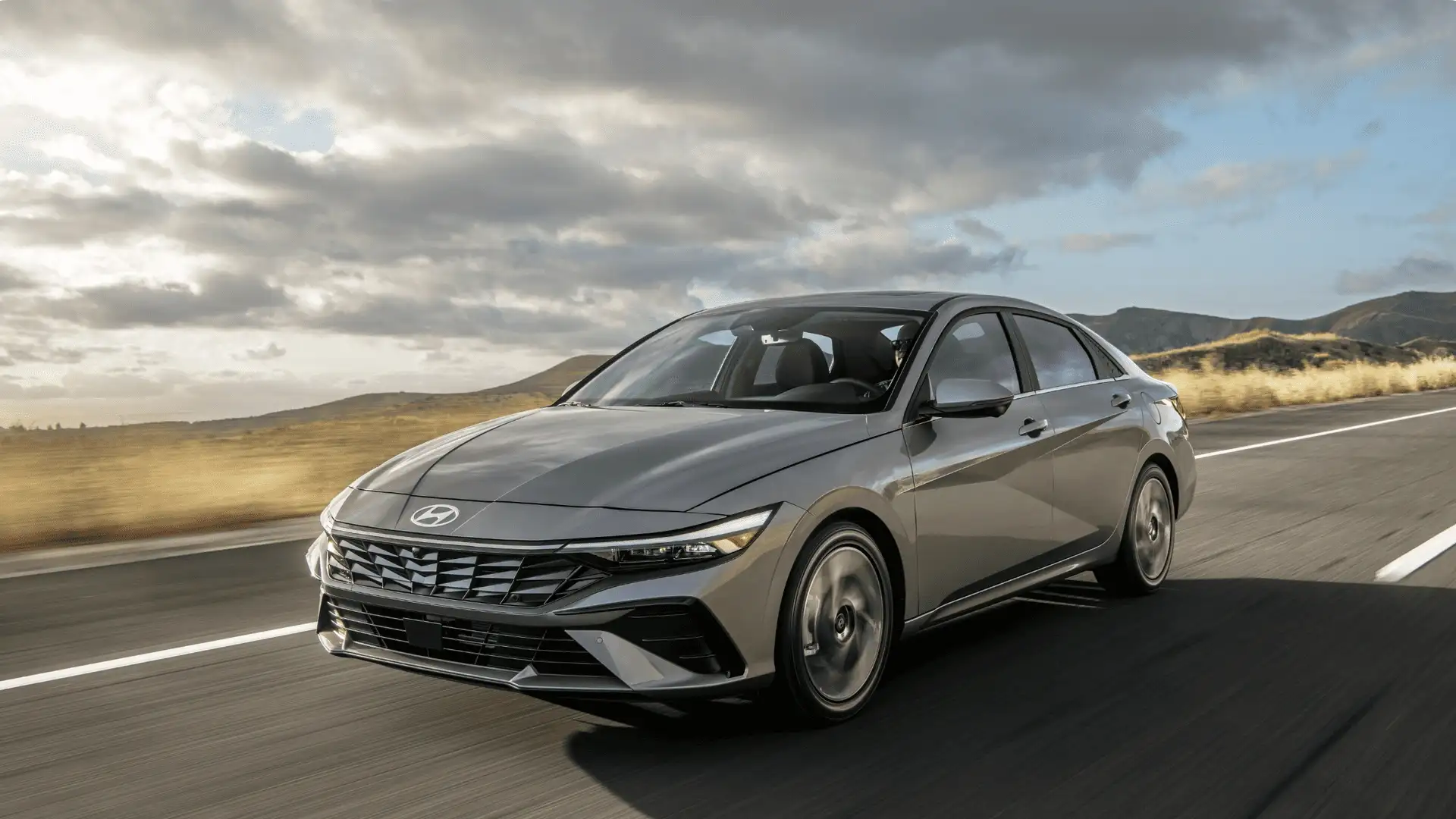2026 Hyundai Elantra driving on open highway in metallic gray with aerodynamic sedan design and motion blur.