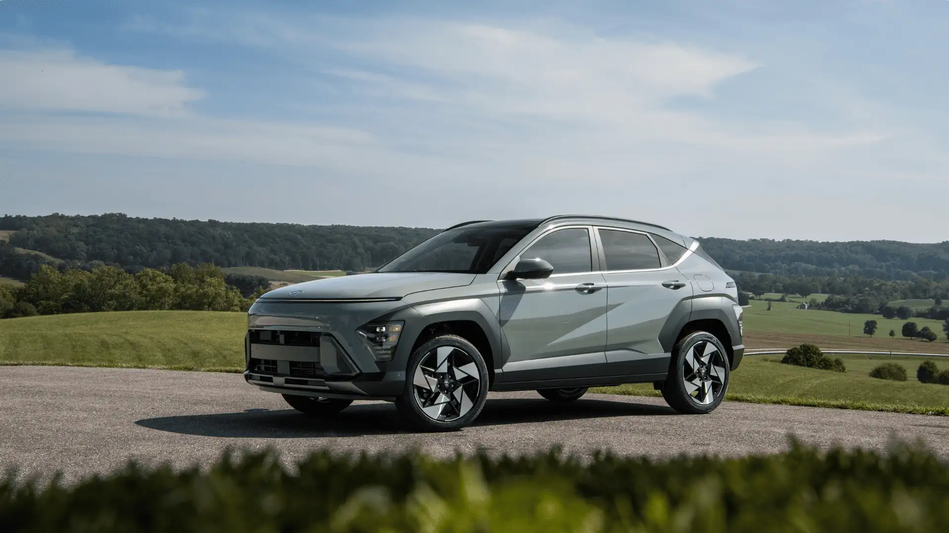 2026 Hyundai Kona shown in side profile on paved road with rolling hills and countryside background.