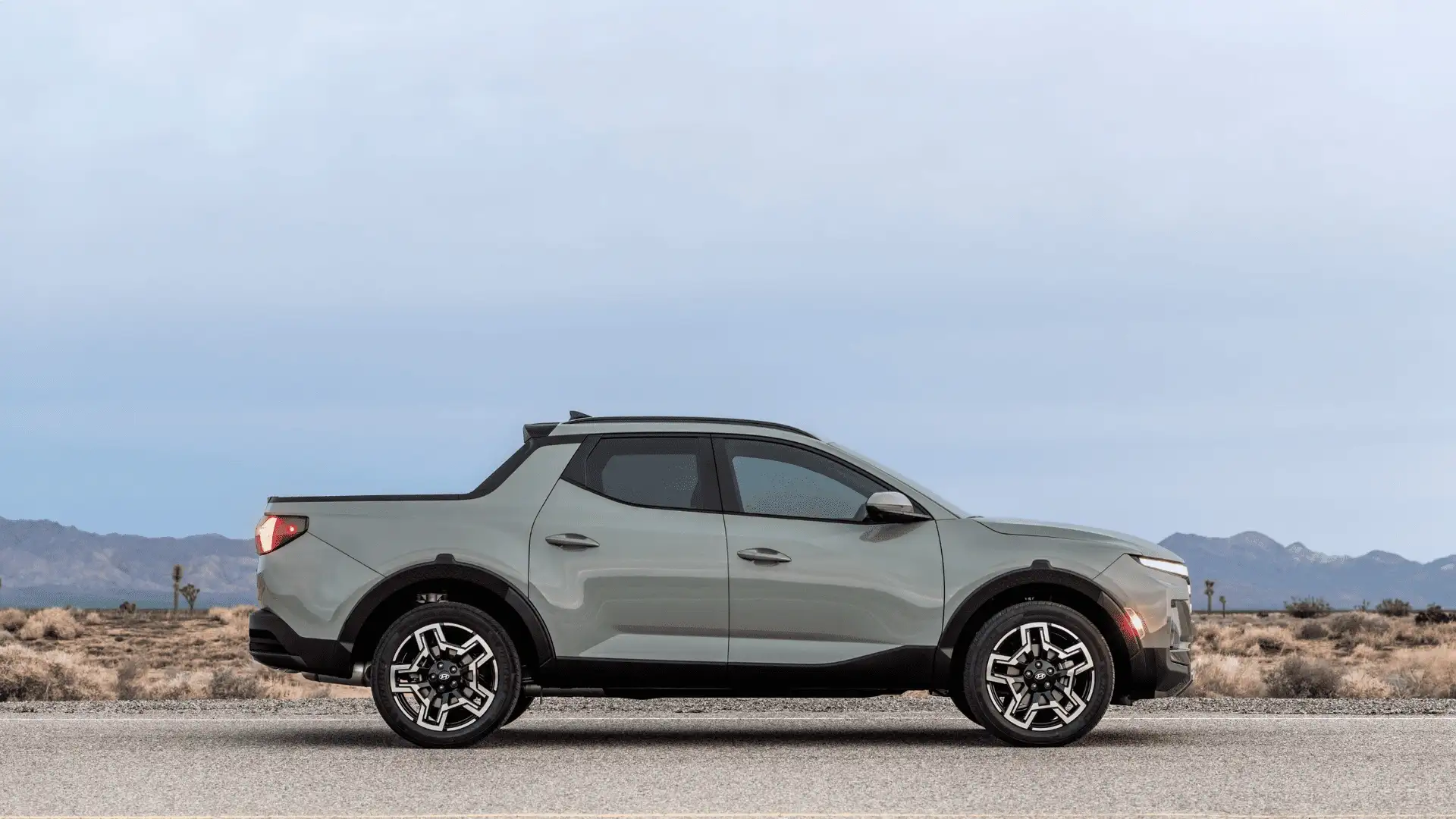 2026 Hyundai Santa Cruz side profile in sage gray showing compact pickup design on desert road.