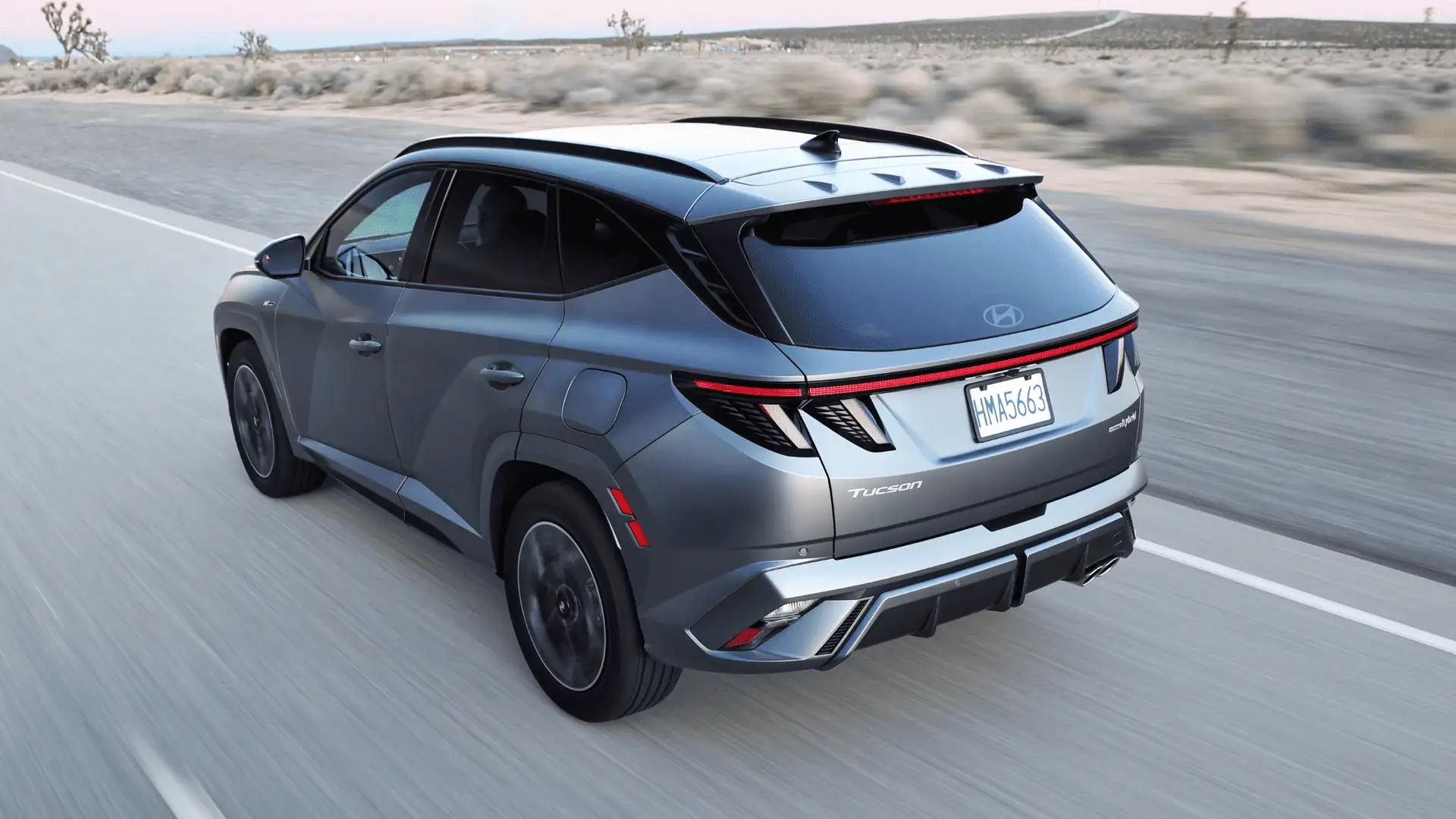 2026 Hyundai Tucson rear three-quarter view driving on open road showcasing LED taillights and sculpted design.