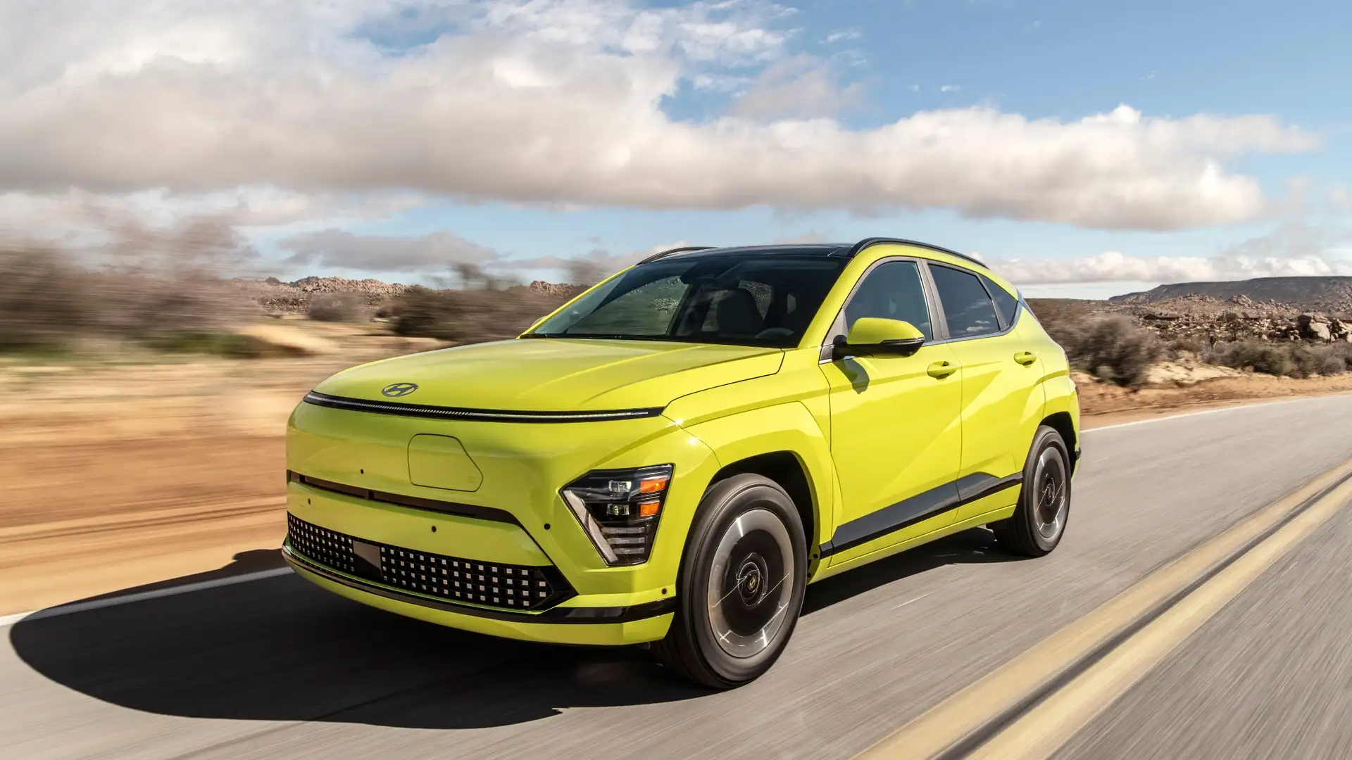 2026 Hyundai Kona Electric driving on a highway with bright green exterior, aerodynamic design, and modern EV styling.