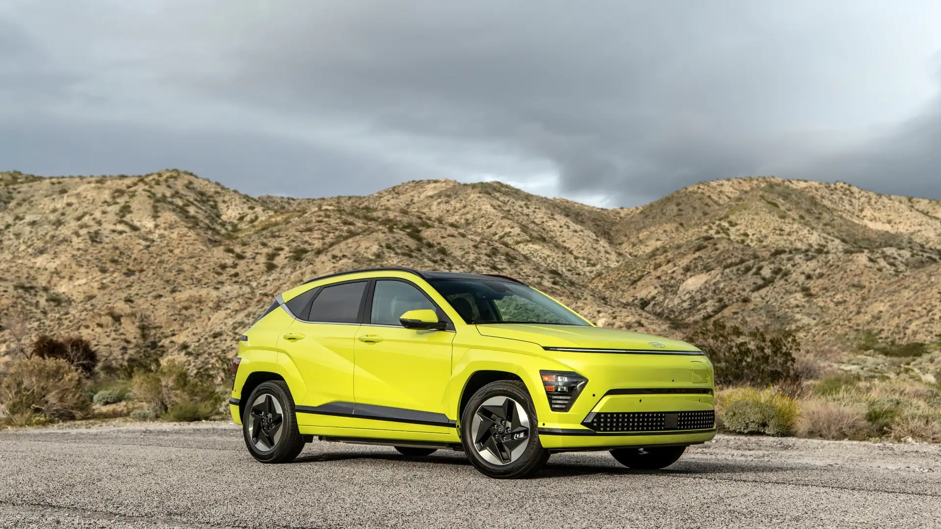 2026 Hyundai Kona Electric compact SUV in bright green shown in three quarter front view on desert road.