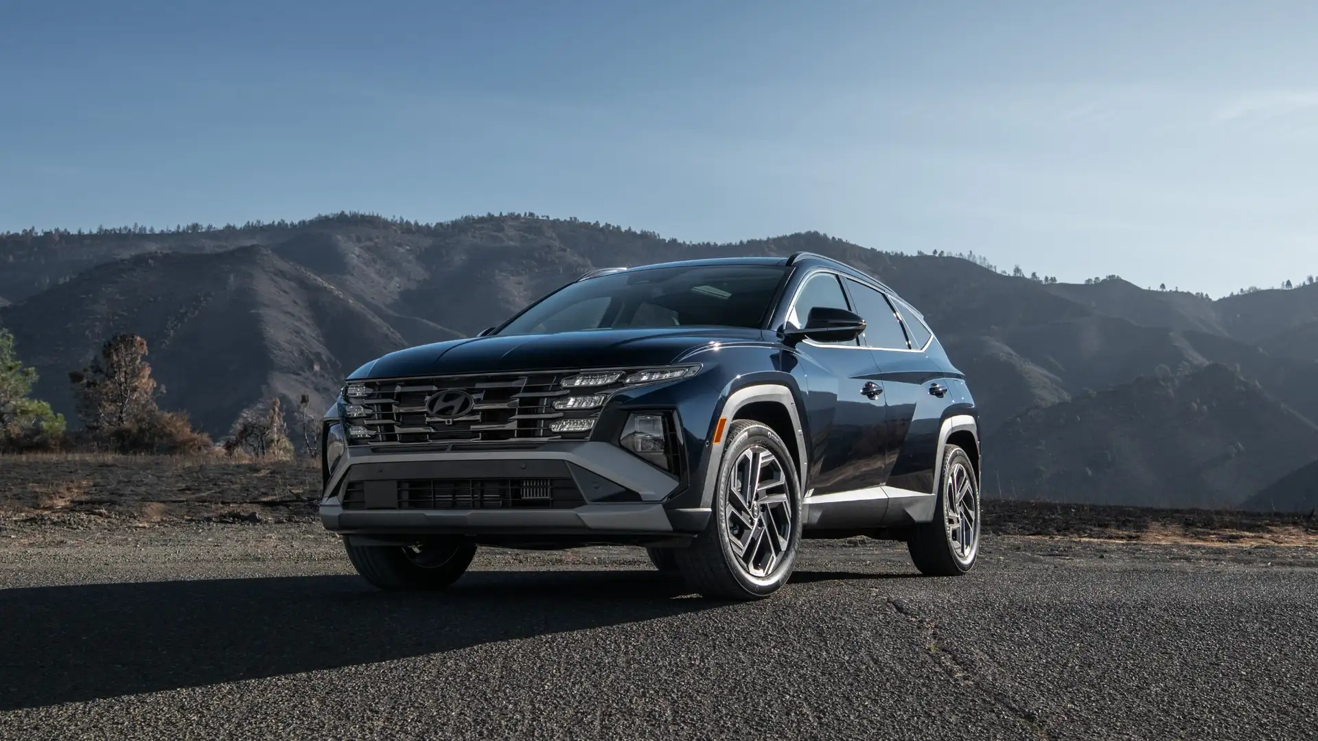 2026 Hyundai Tucson Hybrid SUV parked on a scenic overlook with dark blue exterior, bold grille, and hybrid badging.