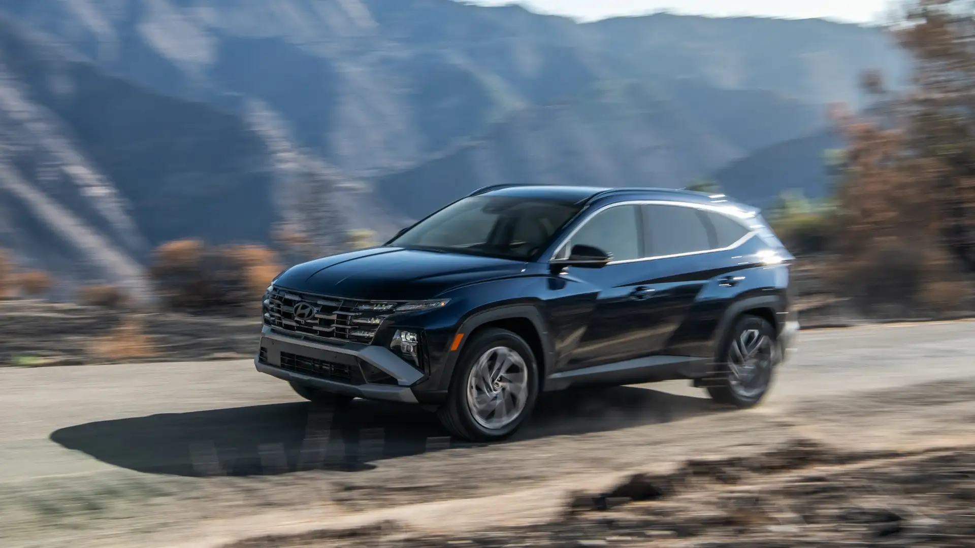 2026 Hyundai Tucson Hybrid SUV driving on mountain road in three quarter front view.